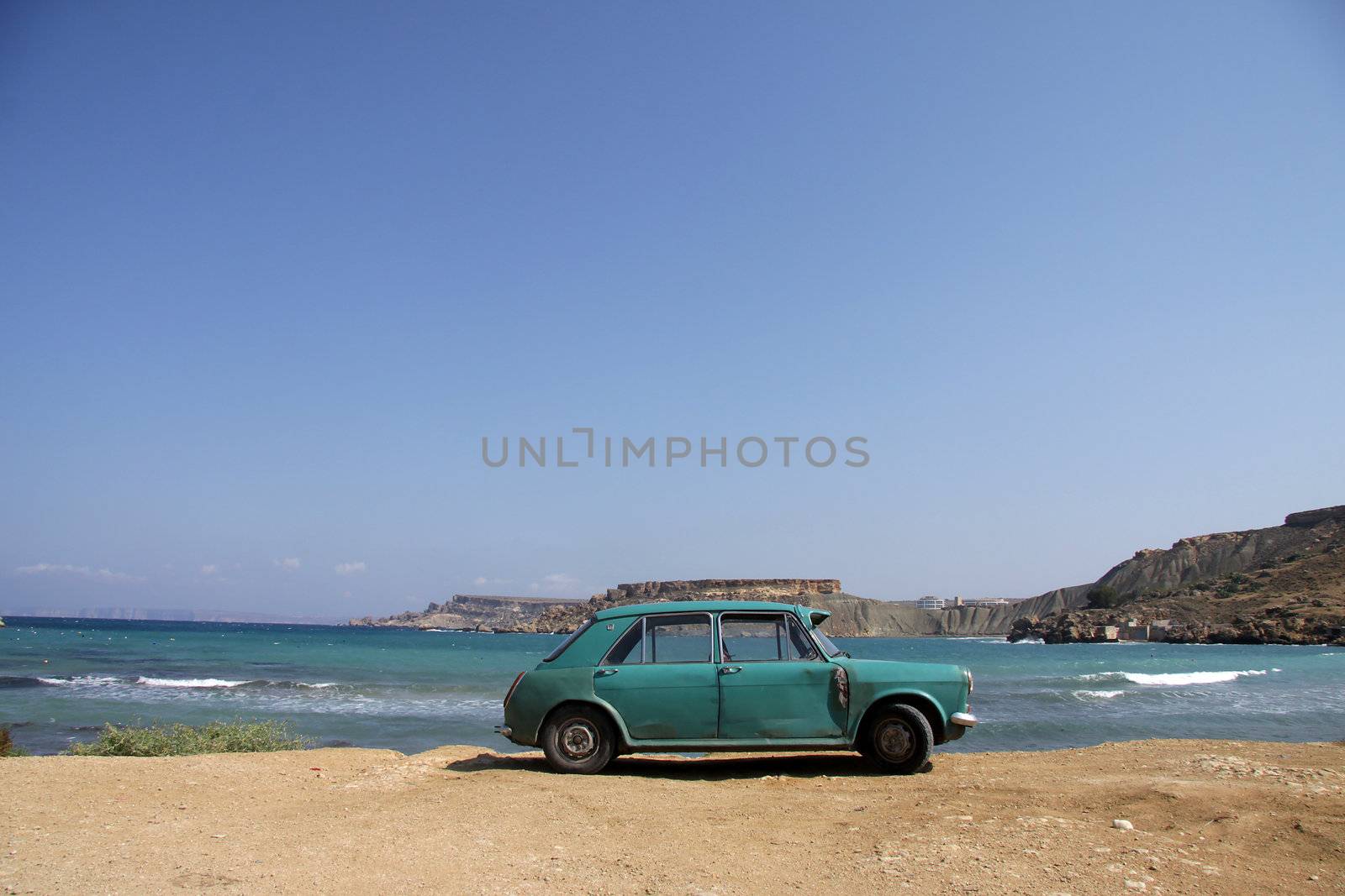 An old green rusty Austin is parked on a scenic beautiful beach