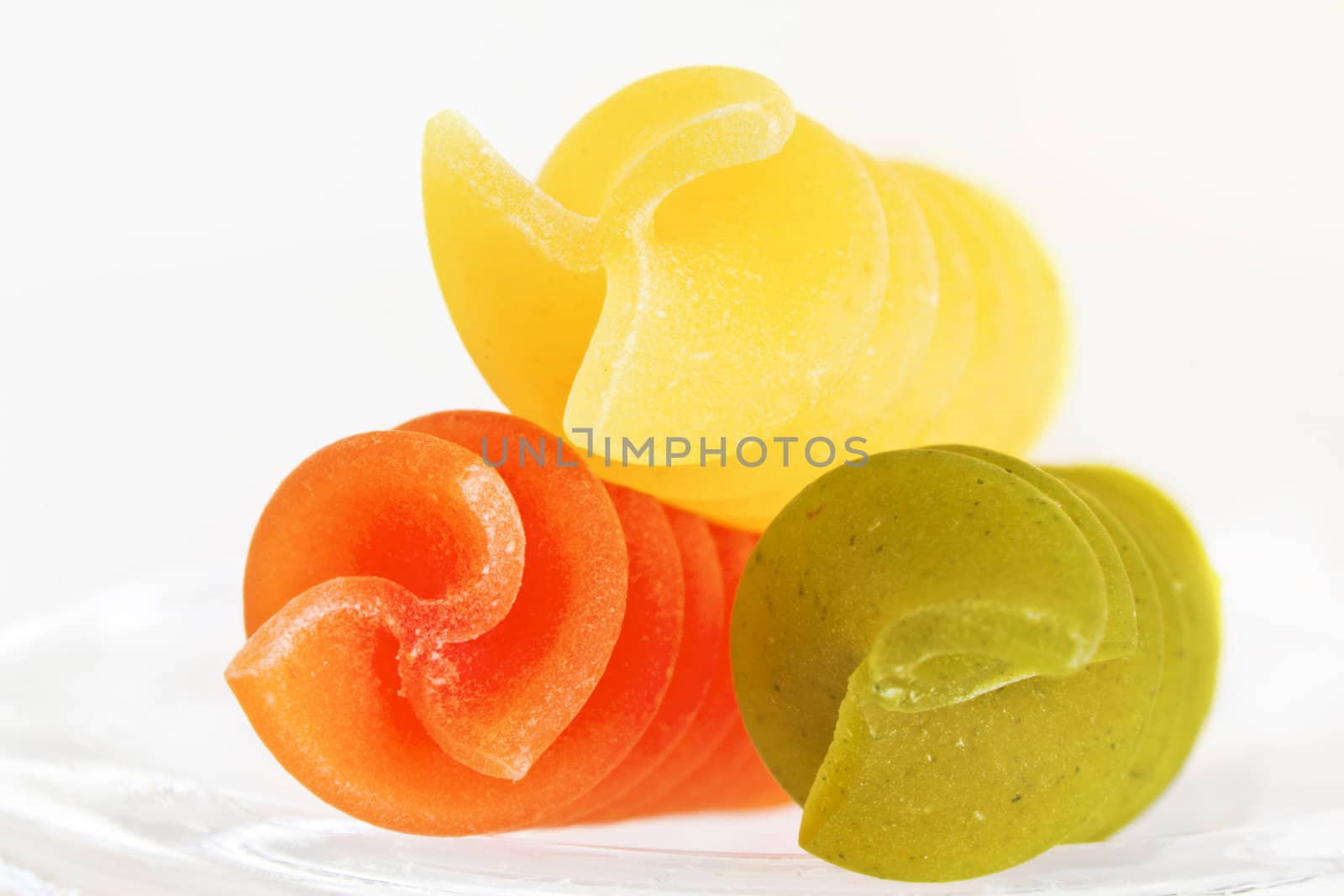 Three colorful raw fusillis on a white background