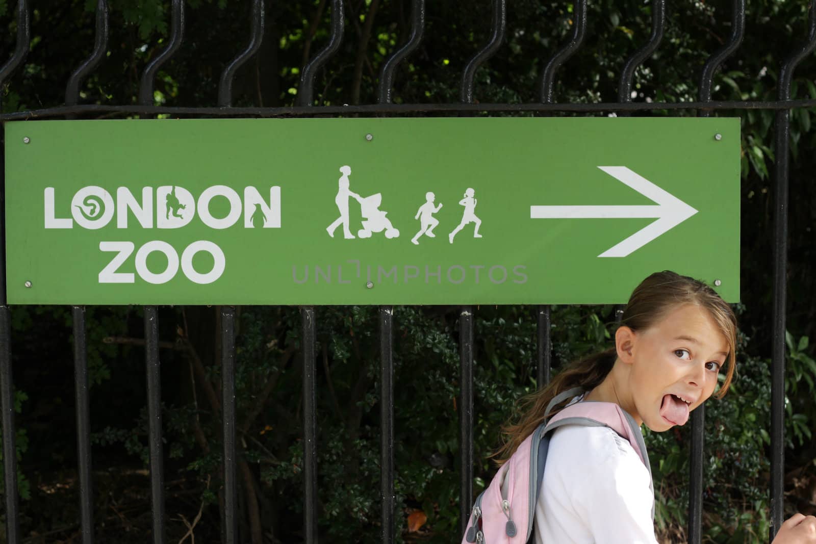 Girl doing a funny face next to a sign showing the way to the zoo