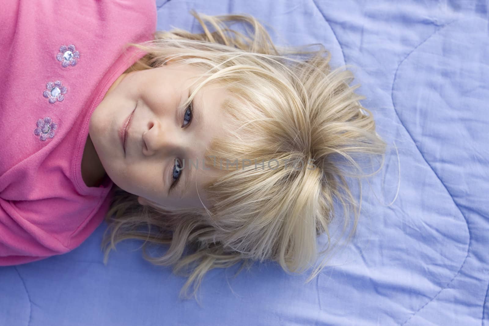 A little girl is lying down on a blue blanket, smiling at the camera. Positive feeling