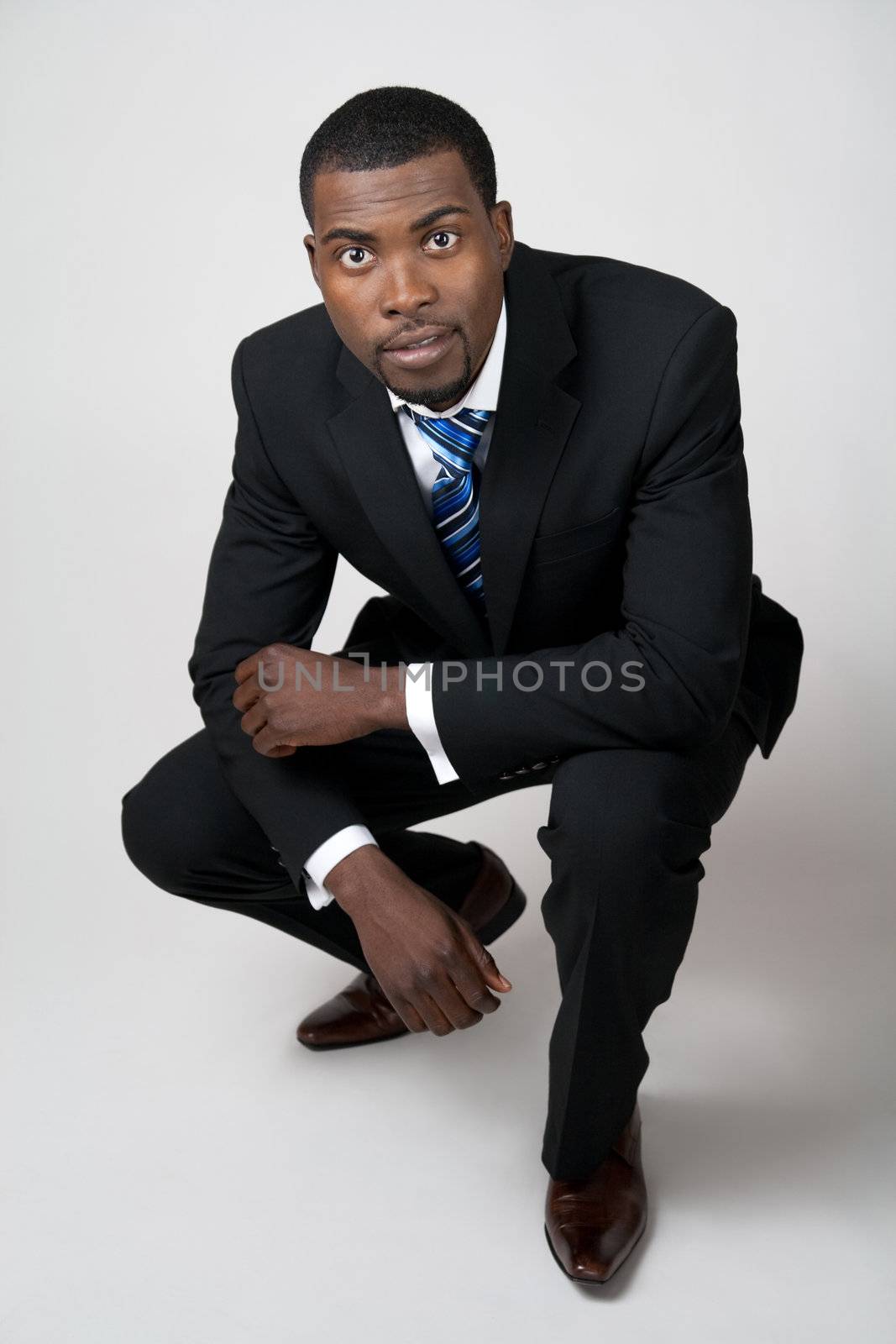 African American business in black suit squatting.