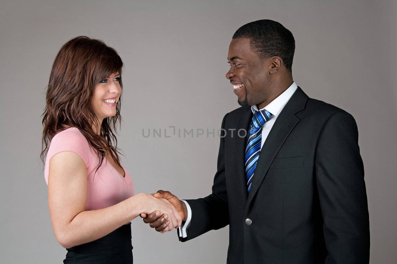 Smiling young woman and African American business man shaking hands.