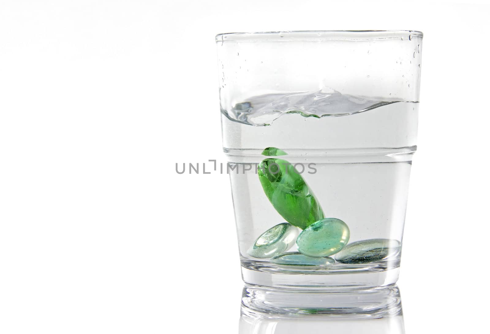 Marbles being dropped in a glass of water. White background isolated image