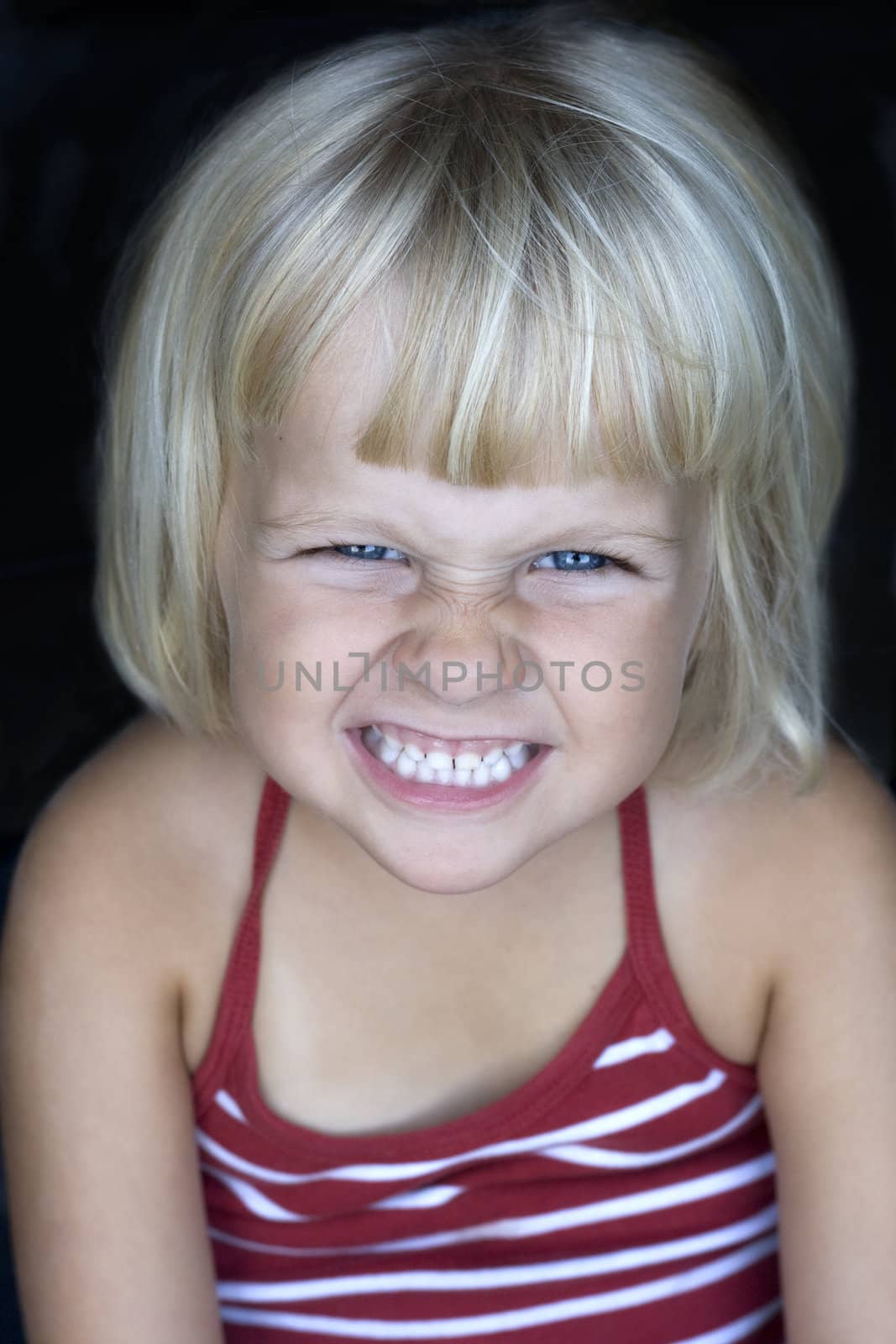 A 4 year old doing a funny face to the camera. Isolated on black.