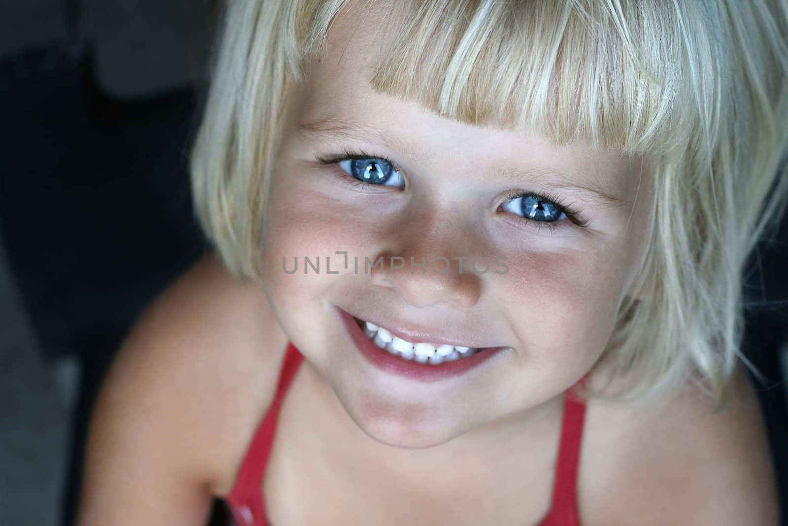 A four year old girl smiling up towards the camera. Horizontal soft image with blurred background