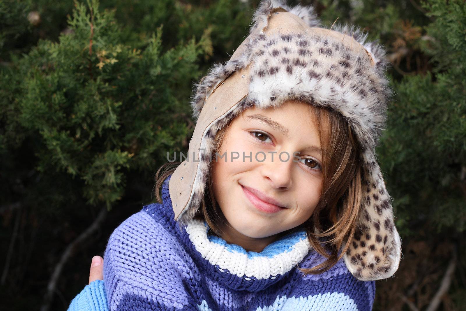 Girl with a fake fur leather hat standing in front of a christmas tree, smiling at the camera. Positive feeling