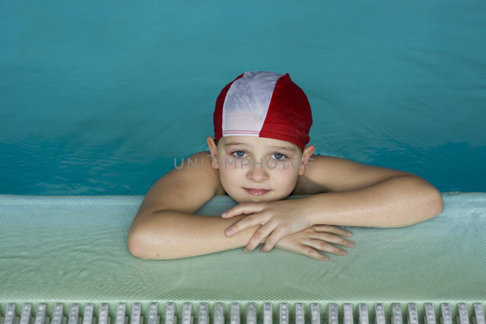 Kid with swimcap on the side of the pool during a swimming lesson