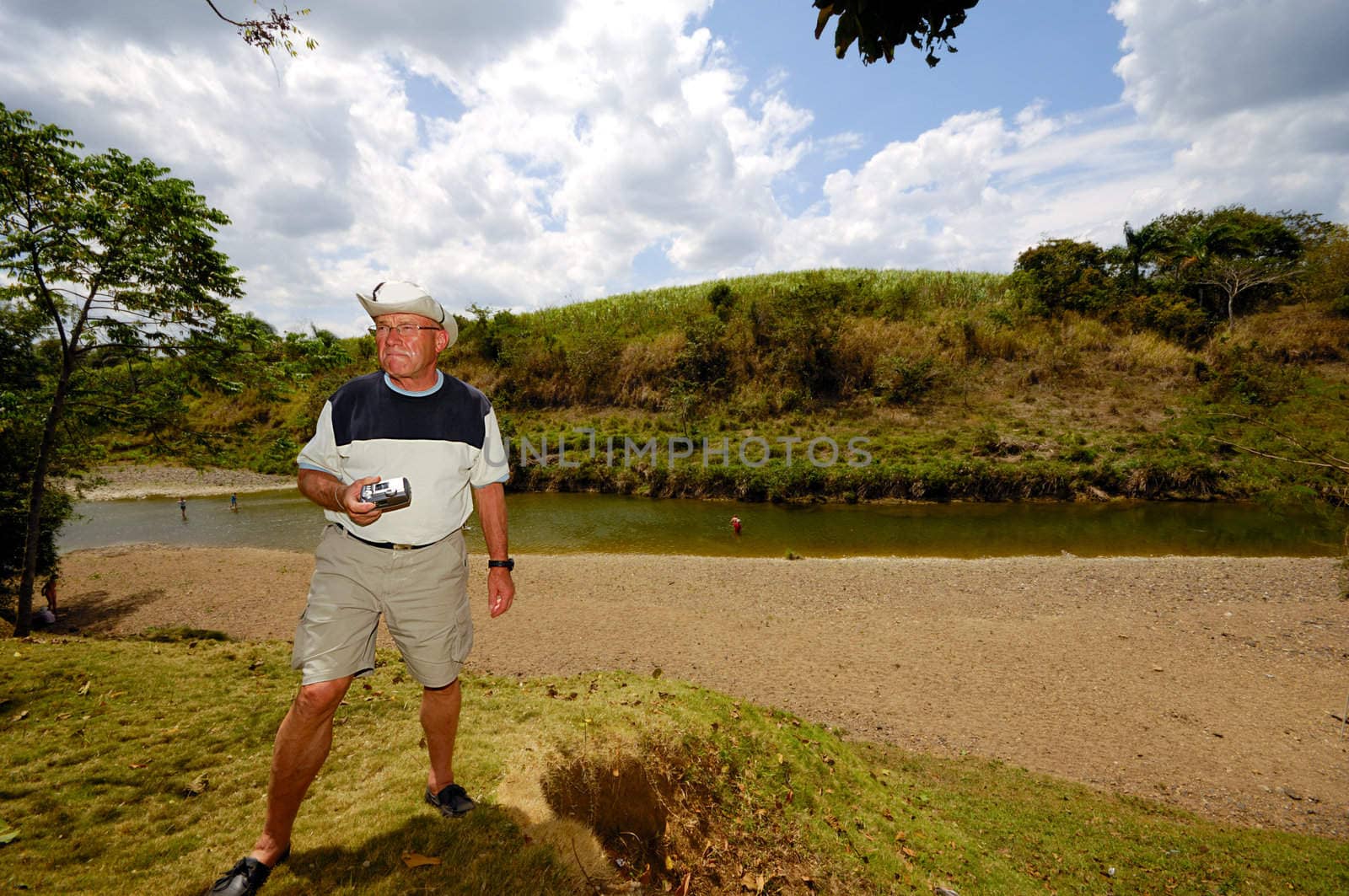 A turist is standing in green nature. The man is a senior and is holding a camera. Dominican Republic.