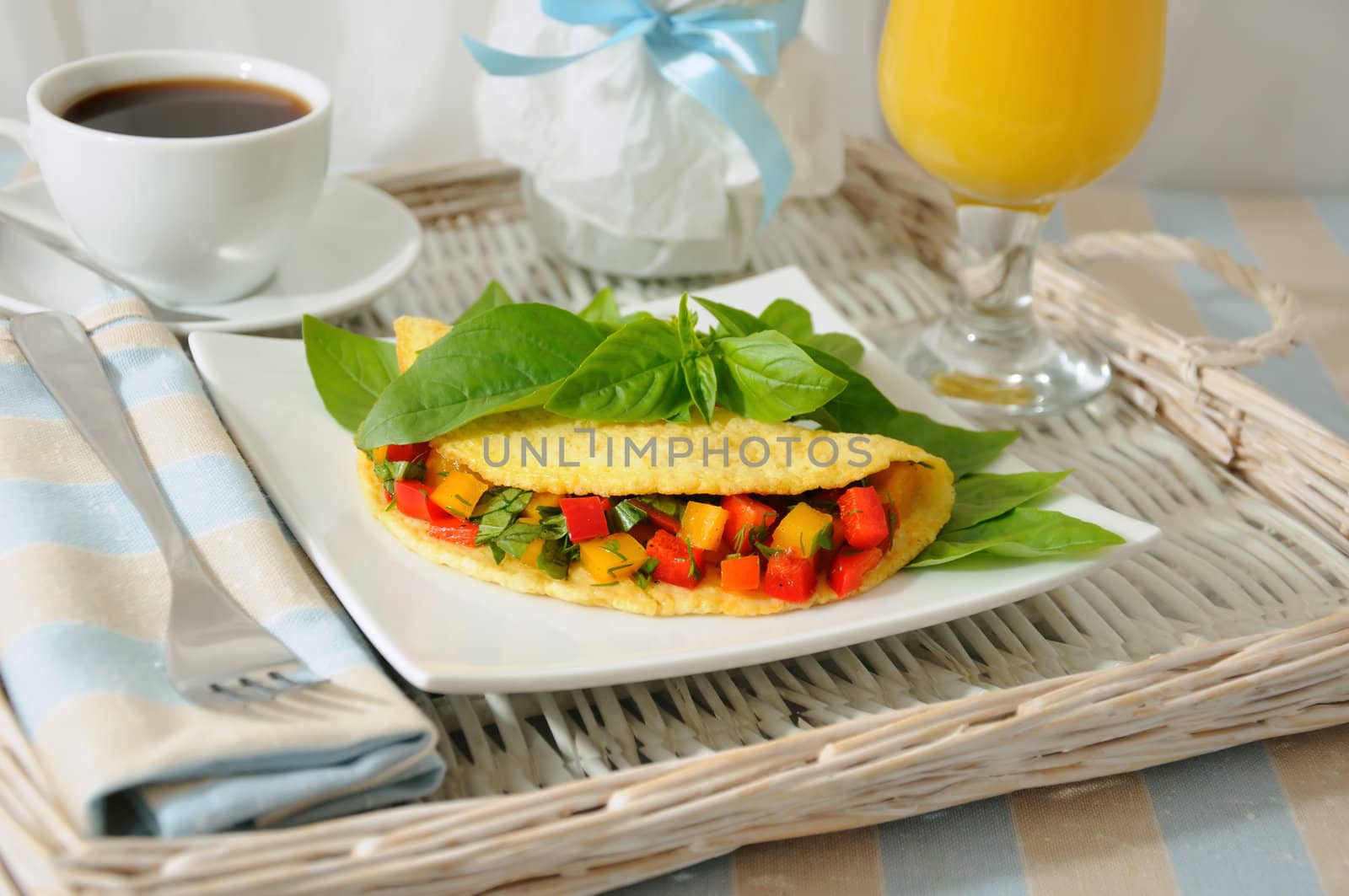 An omelet stuffed with vegetables with basil, orange juice on a tray