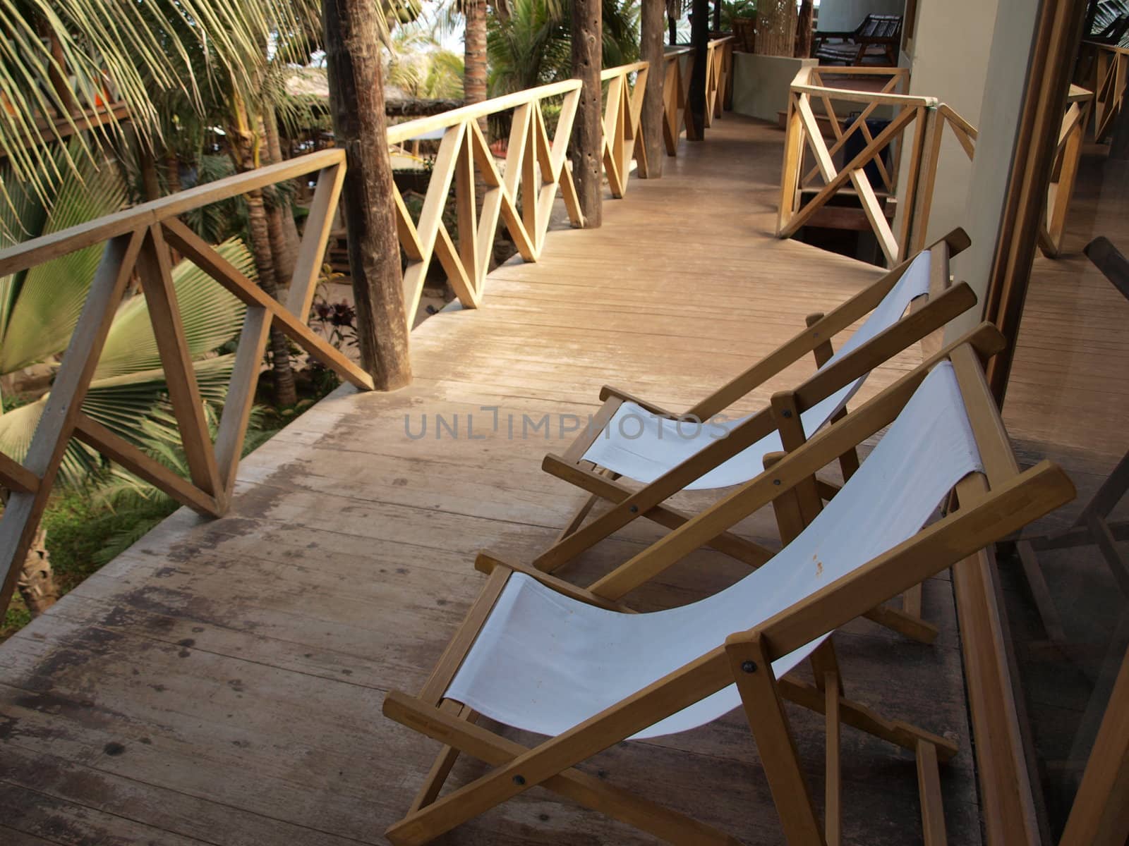 Chairs for suntanning in beach hotel balcony surrounded with palm trees