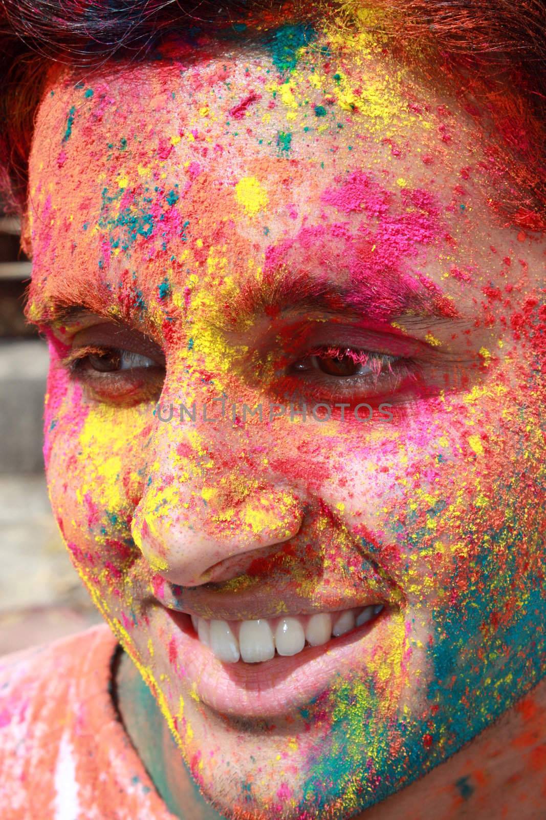 A young Indian guy with his face covered with traditional colors of holi festival.