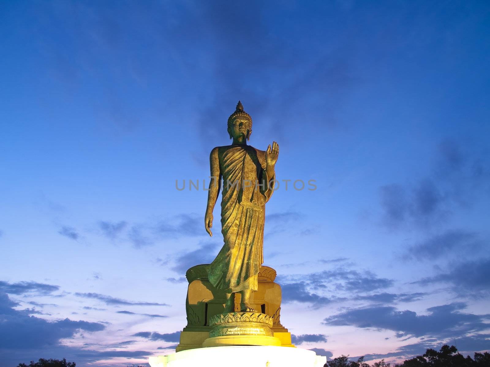 Walking Buddha image in Vitarka Mudra posture illuminate with spotlight at twilight time, Buddhamonthon, Nakhon Pathom, Thailand