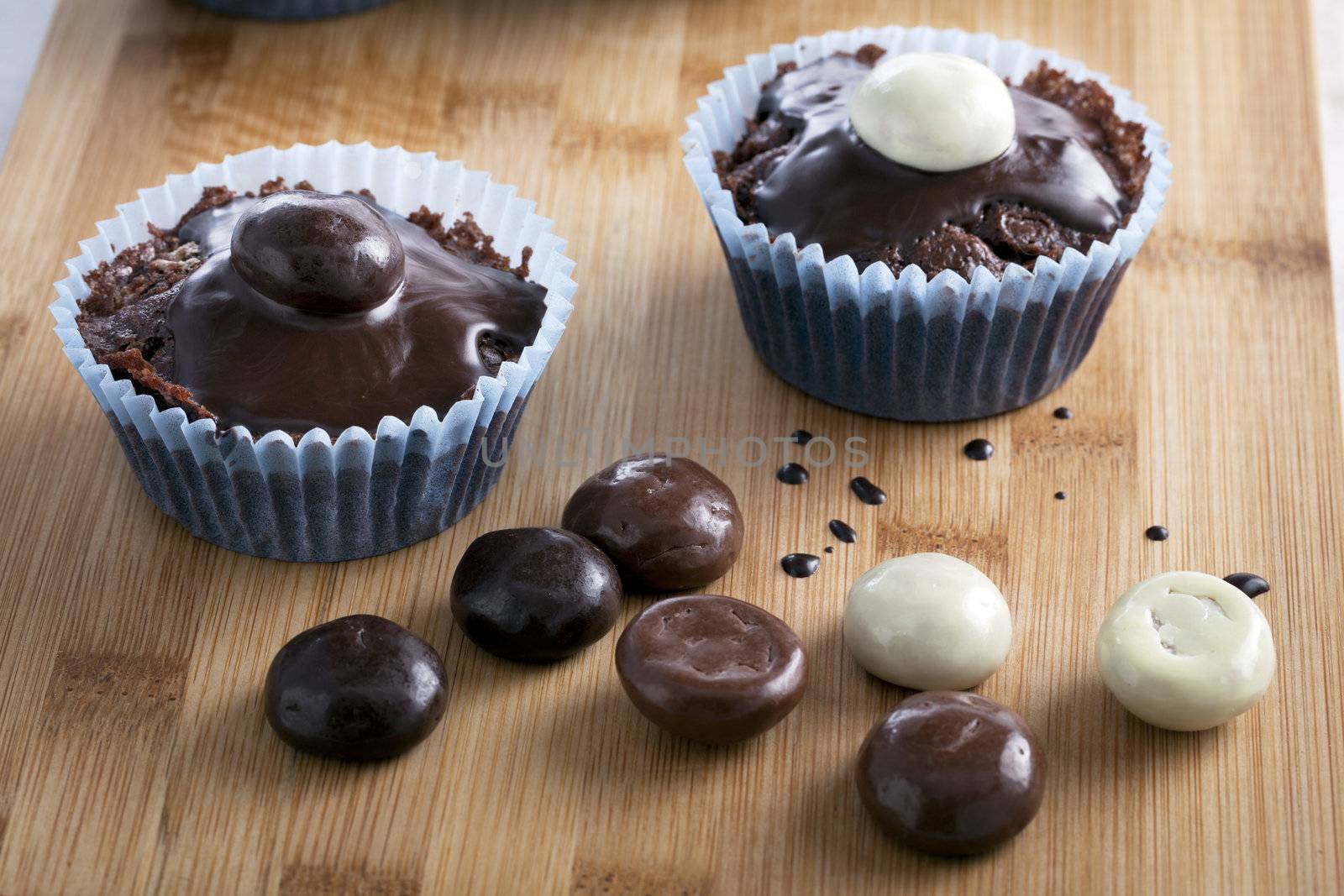 Two chocolate cupcakes topped with chocolate sauce and chocolate covered candies.