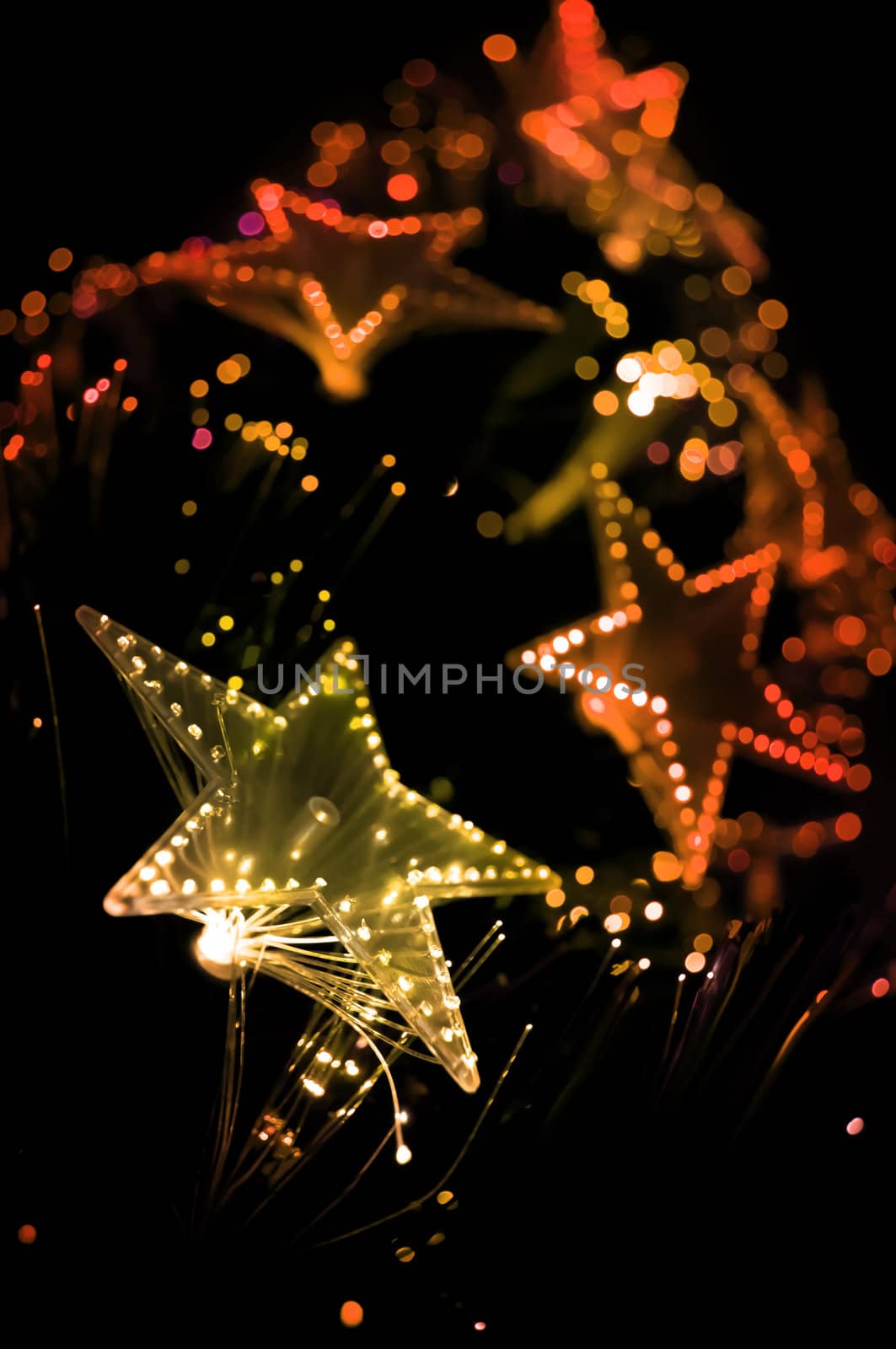 A view from the base of a Christmas tree with illuminated golden, orange and red lights. Focus on foreground lights with black background.
