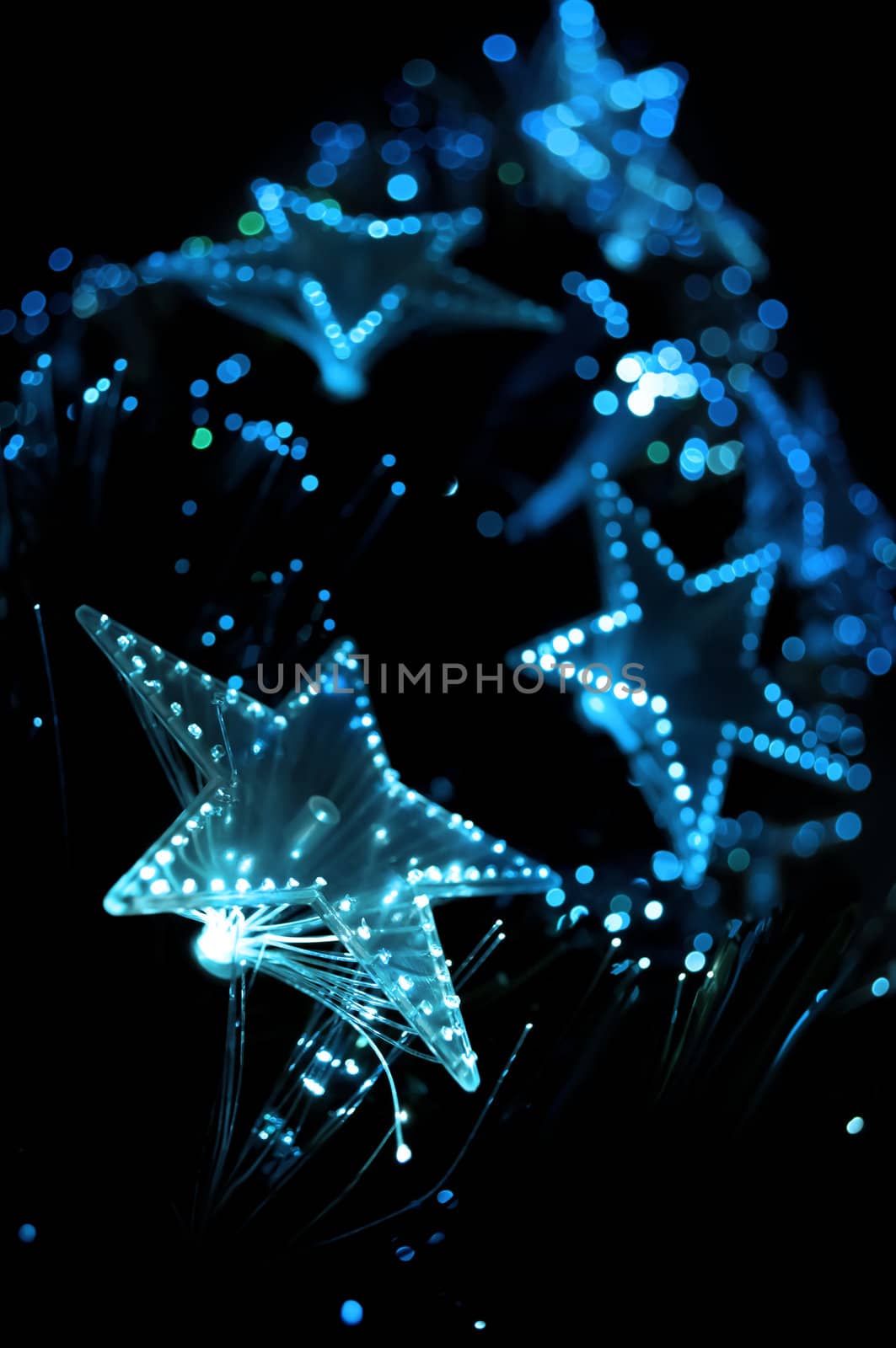 A view from the base of a Christmas tree with illuminated blue lights. Focus on foreground lights with black background.