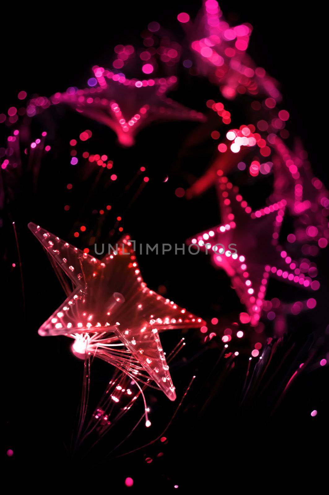 A view from the base of a Christmas tree with illuminated pink and red lights. Focus on foreground lights with black background.