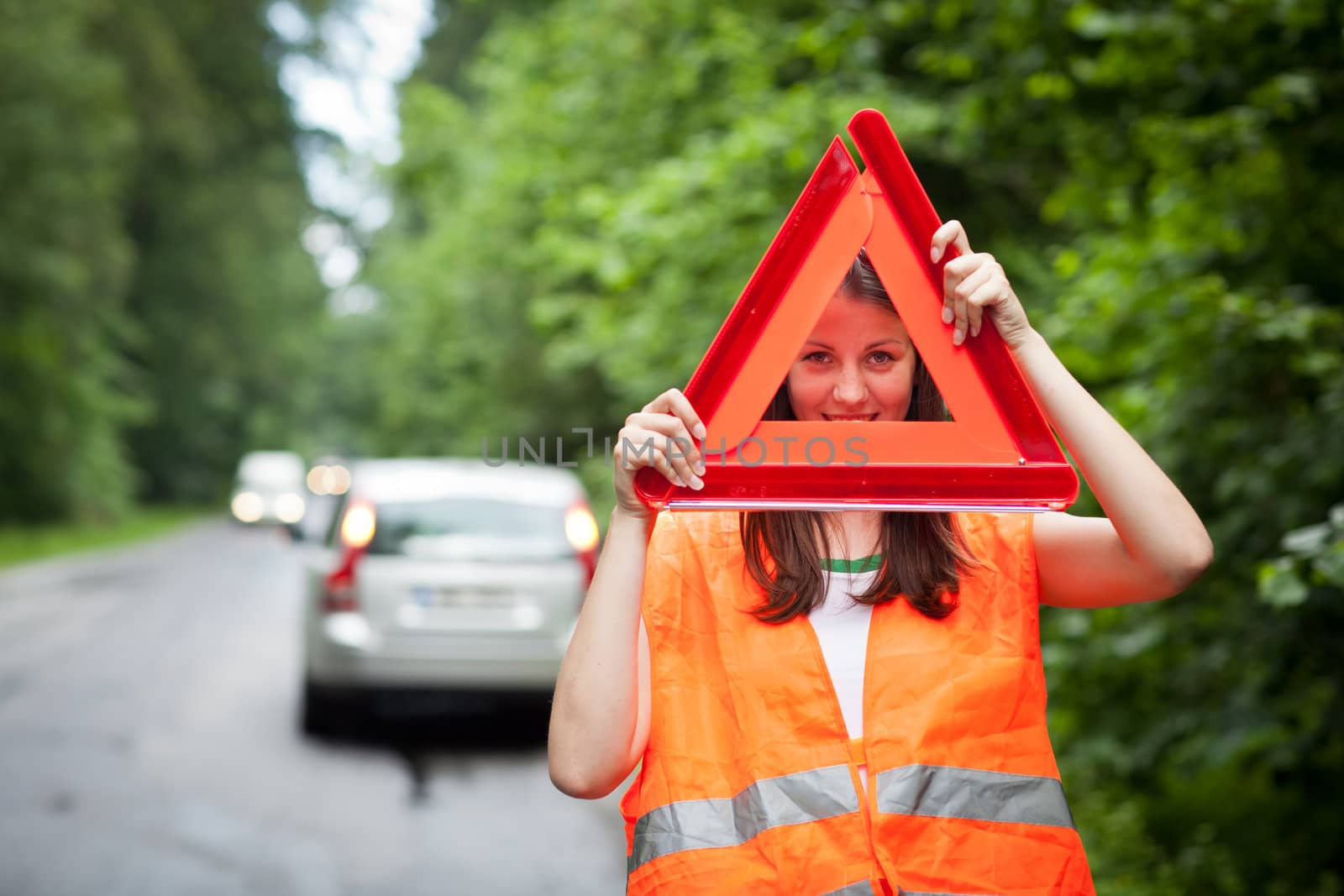 Young female driver wearing a high visibility vest, calling the roadside service/assistance after her car has broken down