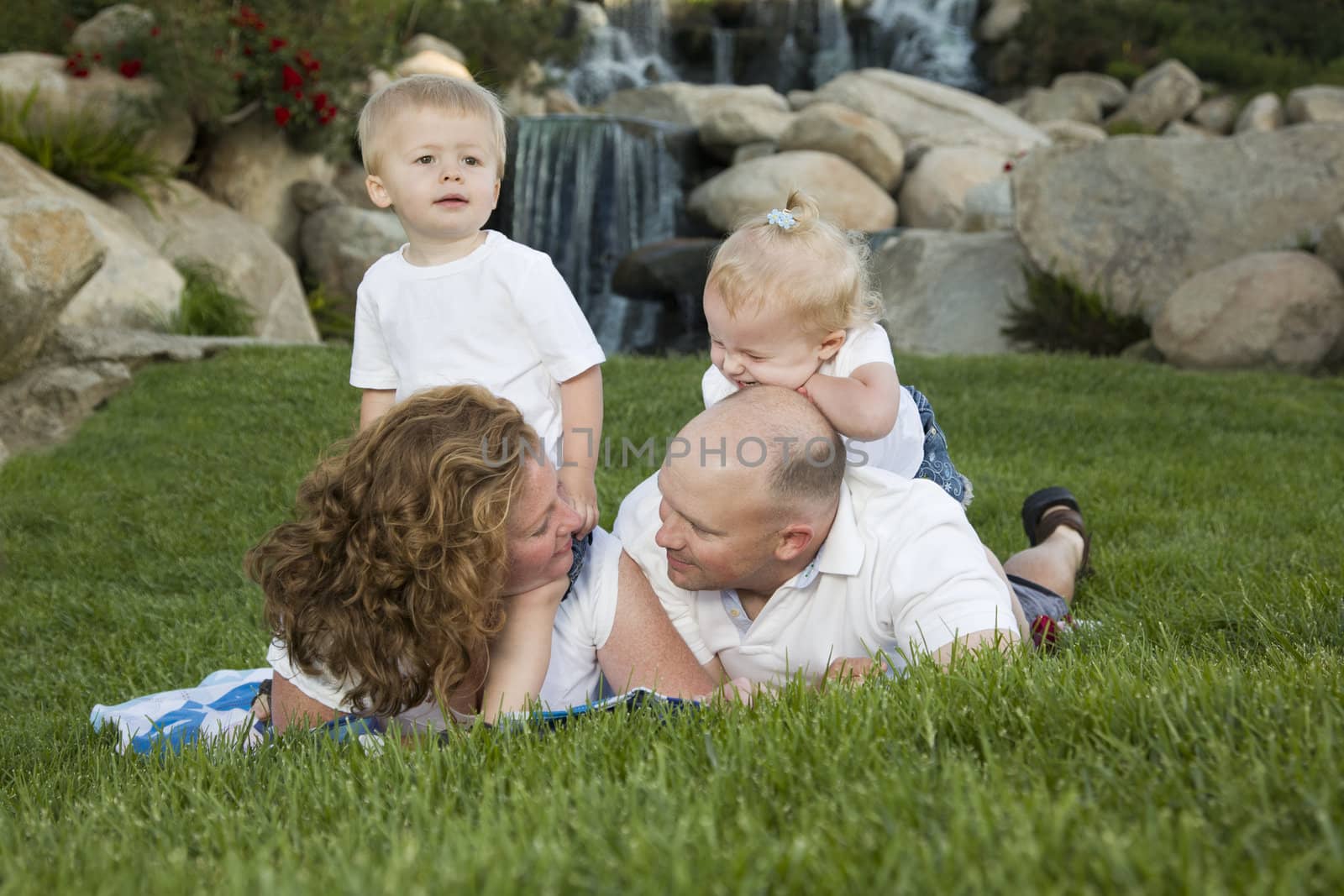 Affectionate Couple Gaze at each other as Cute Twins Look On at the Park Near Waterfall.