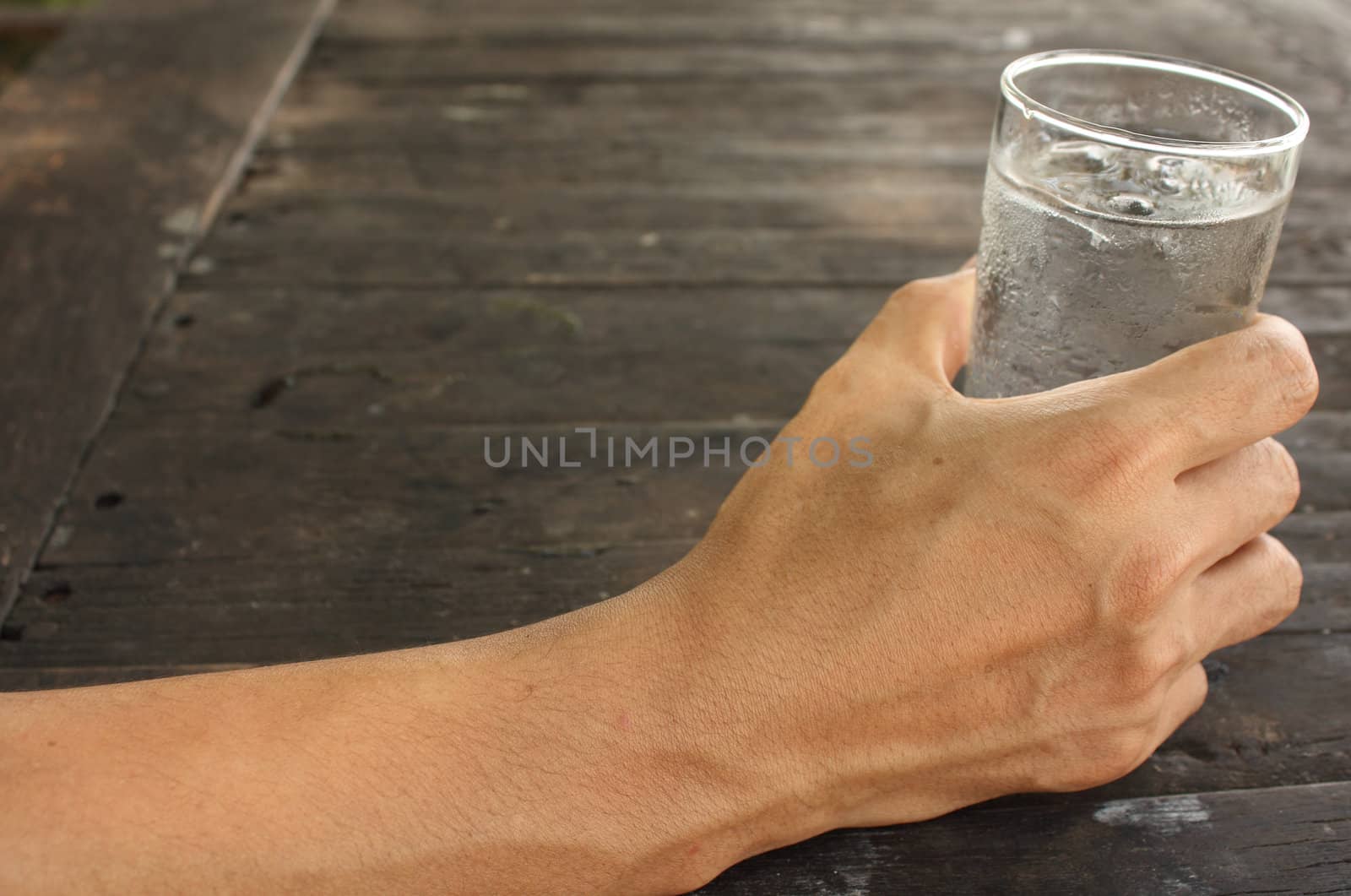 Man hand holding a glass of water on wood background