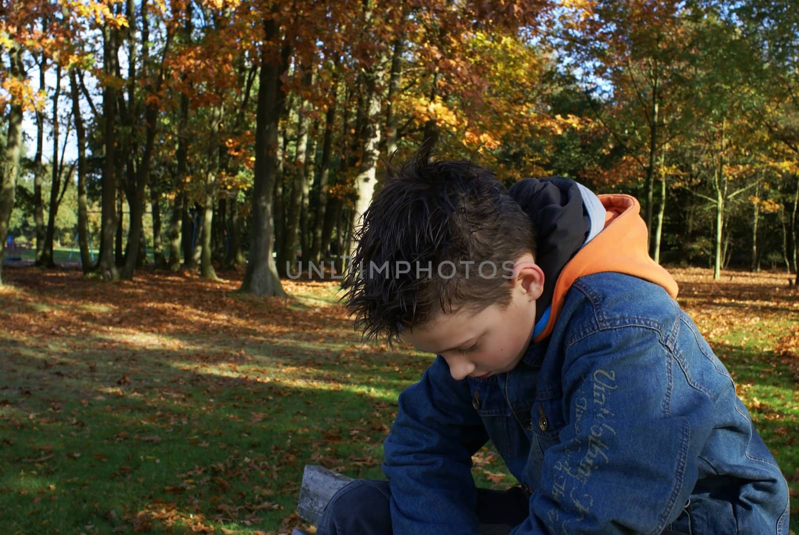 Sad young boy sitting in the park.