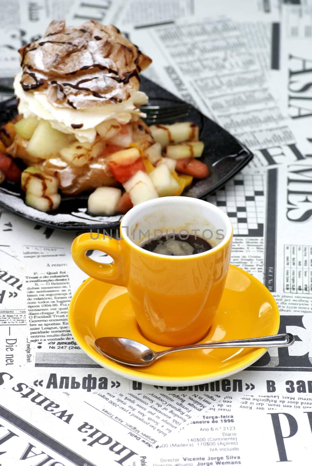 A cup of coffee in front of some confectionery, standing on a 'newspaper table'.