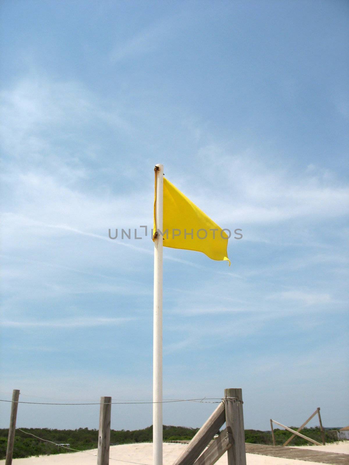 A yellow caution flag posted in the sand at the beach.