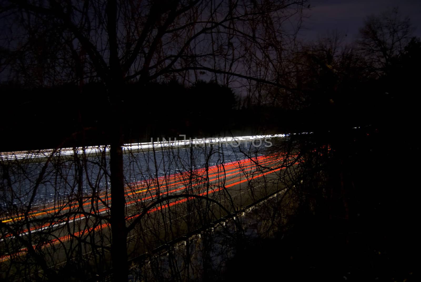 A nighttime highway shot using slow shutterspeed - glowing light trails are visible through the trees.