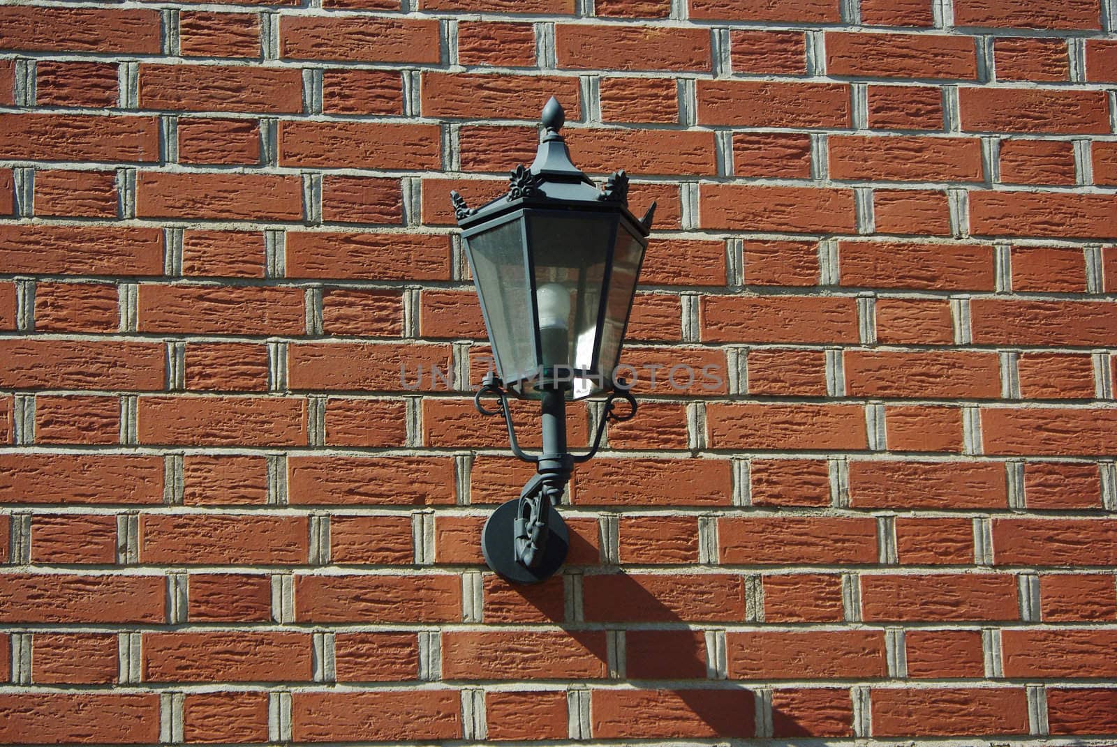 A brass quadrilateral stylish lantern attached to a brick wall.