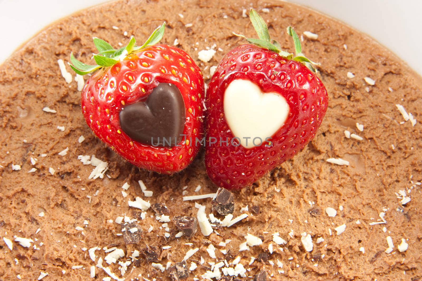 Picture of two strawberries with a heart center laying on  chocolate mousse