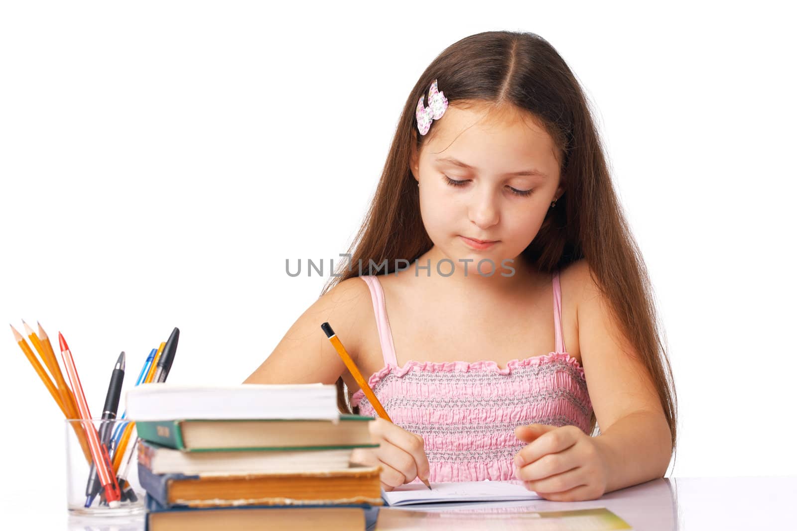 Cute little girl writing something in the copybook with pencils and books near it.