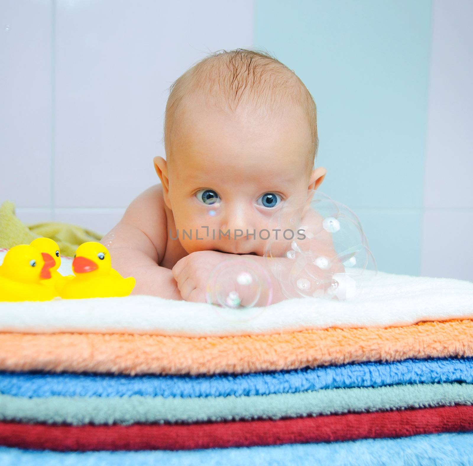 Little cute boy with soap bubbles lying on colorful towels by maxoliki