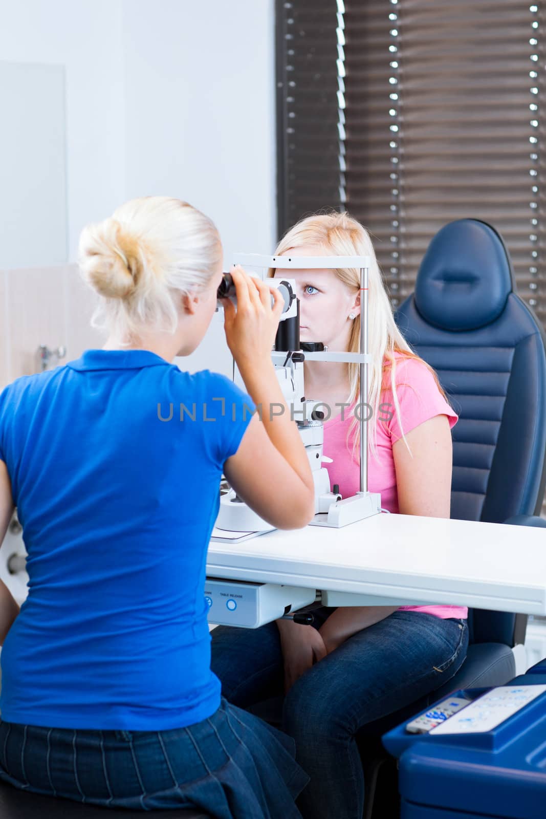 optometry concept - pretty, young female patient having her eyes examined by an eye doctor (color toned image; shallow DOF)