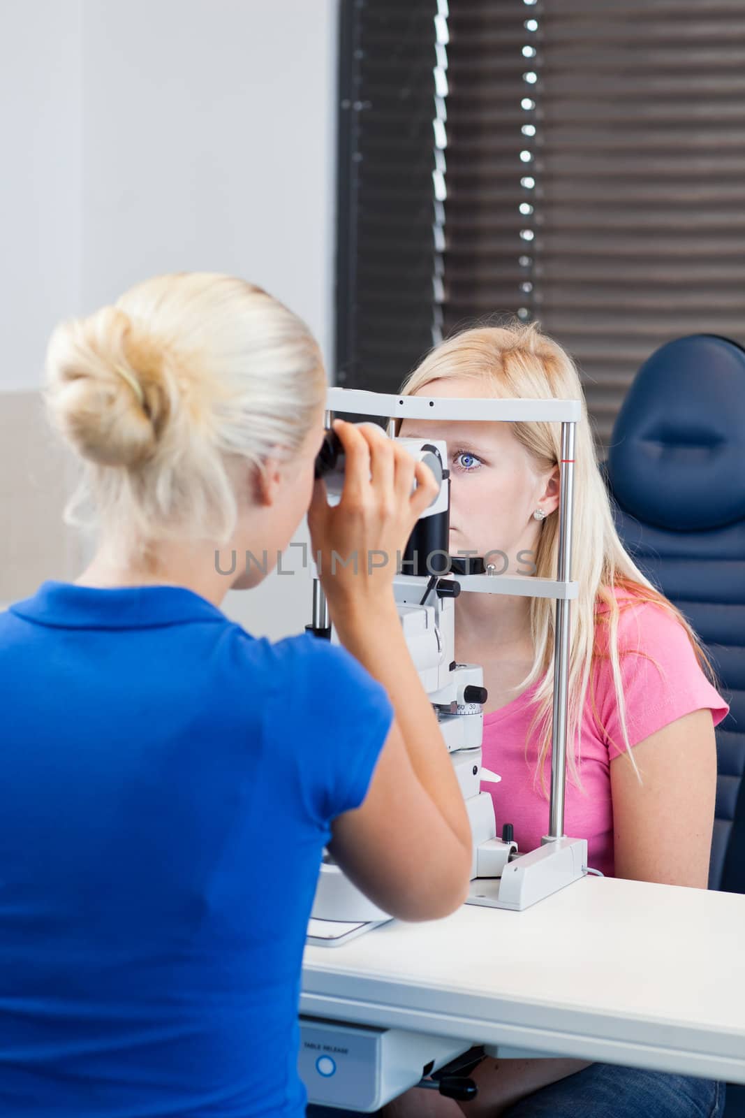 optometry concept - pretty, young female patient having her eyes examined by an eye doctor (color toned image; shallow DOF)