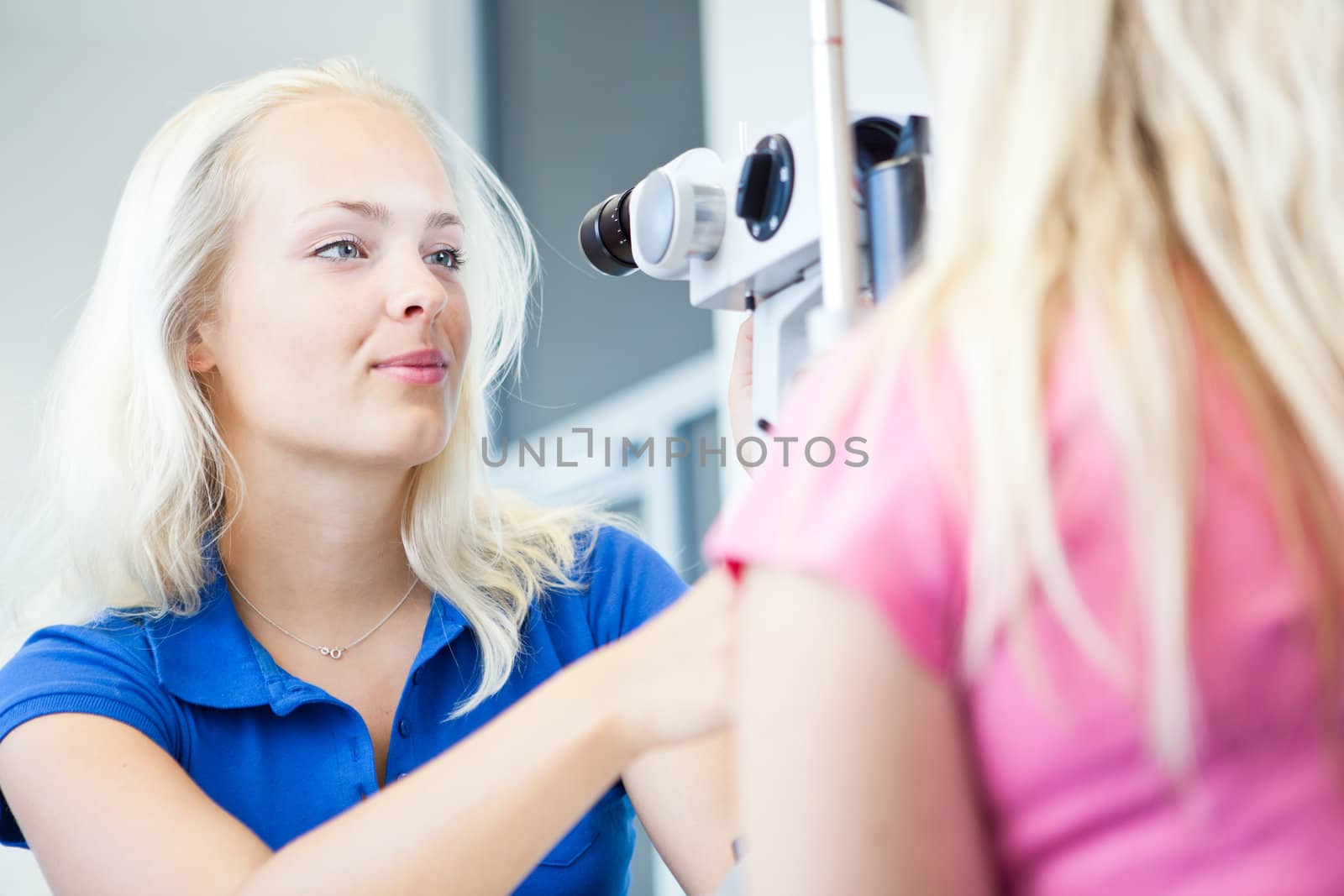 optometry concept - pretty, young female patient having her eyes examined by an eye doctor (color toned image; shallow DOF)