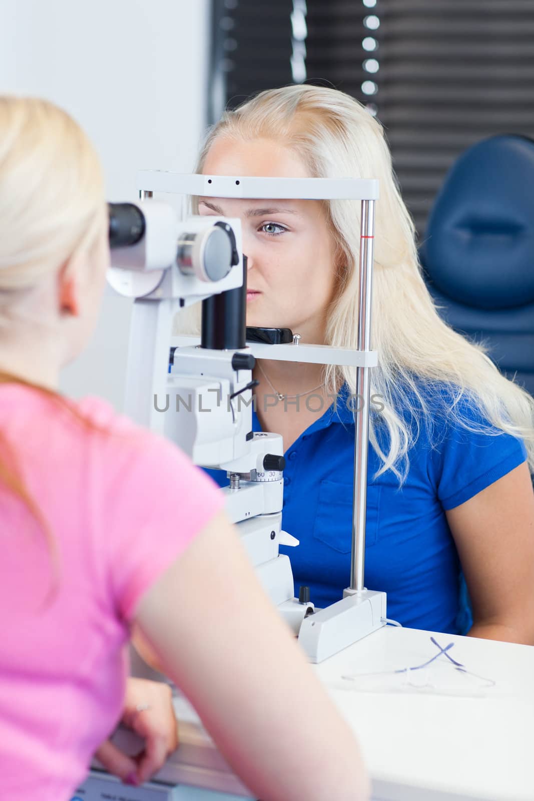 optometry concept - pretty, young female patient having her eyes examined by an eye doctor (color toned image; shallow DOF)