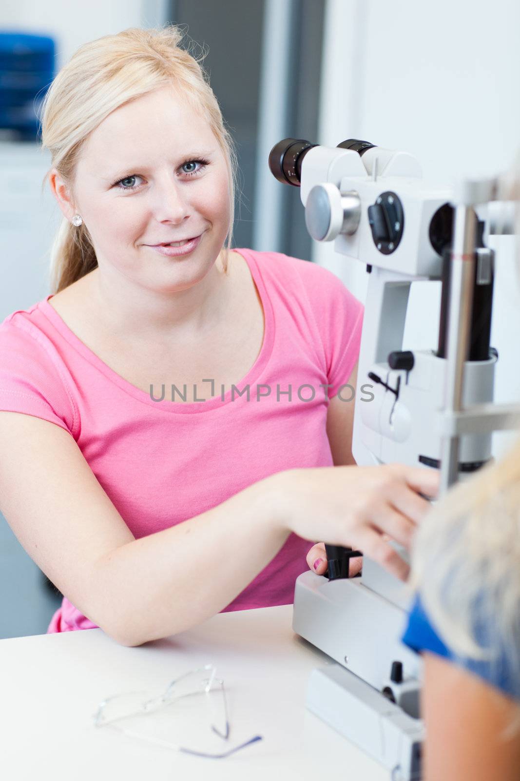 optometry concept - pretty, young female patient having her eyes examined by an eye doctor (color toned image; shallow DOF)