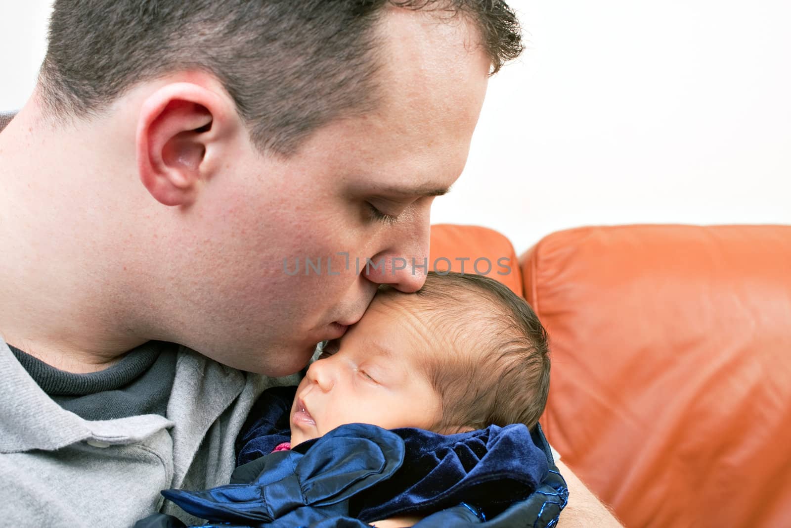 A newborn baby is held by her dad as he kisses her cheek.