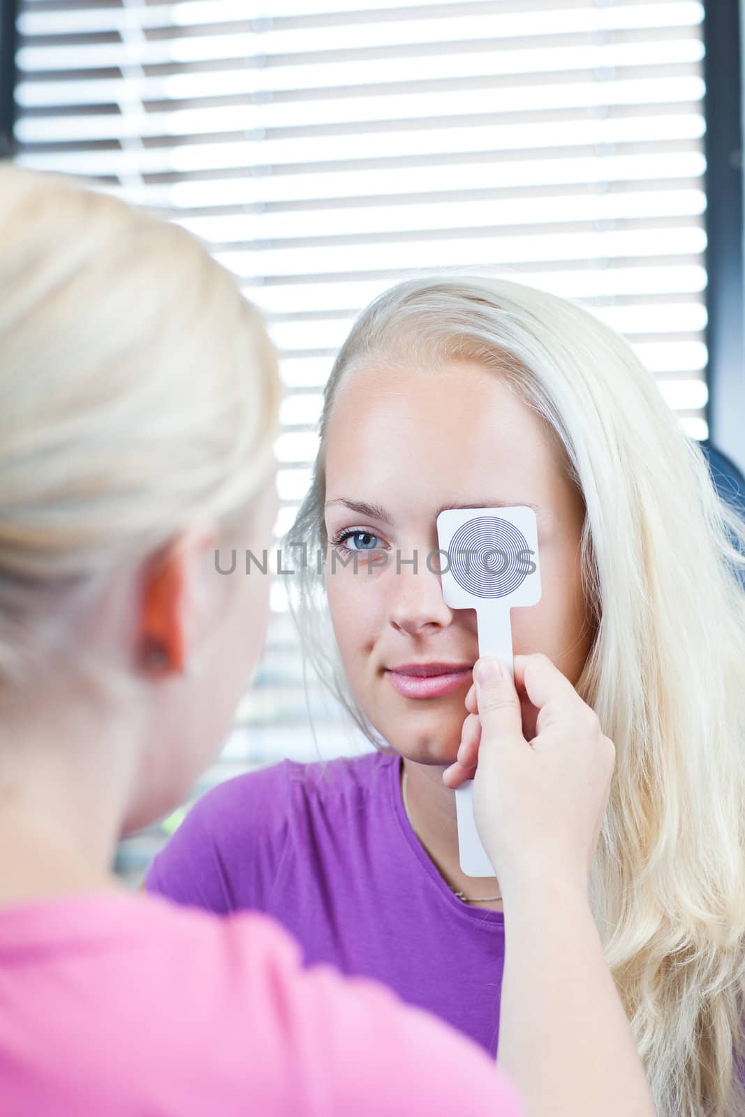 optometry concept - pretty, young female patient having her eyes examined by an eye doctor (color toned image; shallow DOF)