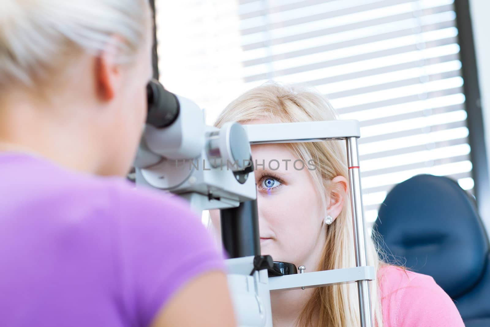 optometry concept - pretty, young female patient having her eyes examined by an eye doctor (color toned image; shallow DOF)