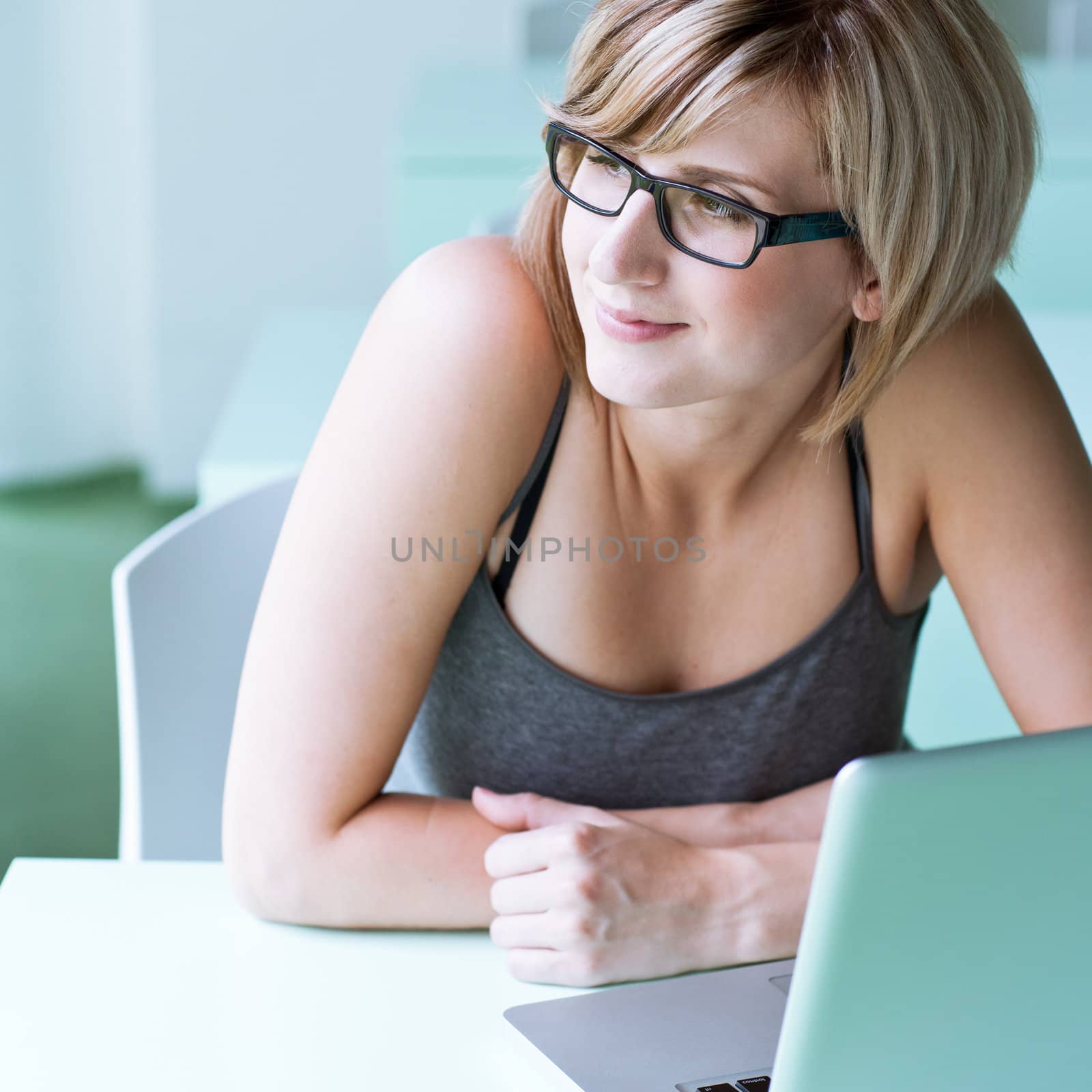 Portrait of a young woman pensively looking out of the window while sitting in front of her laptop