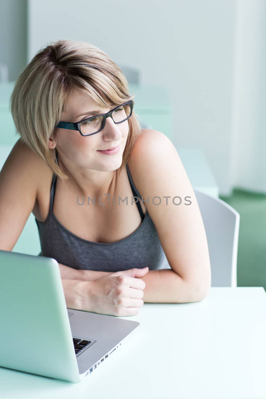 Portrait of a young woman pensively looking out of the window while sitting in front of her laptop