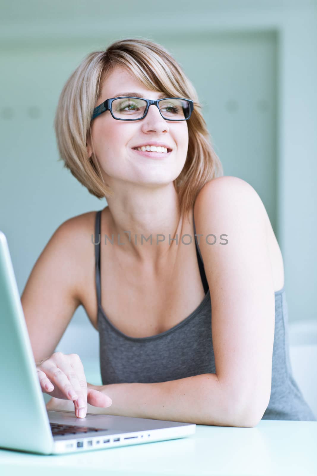 Portrait of a young woman pensively looking out of the window while sitting in front of her laptop