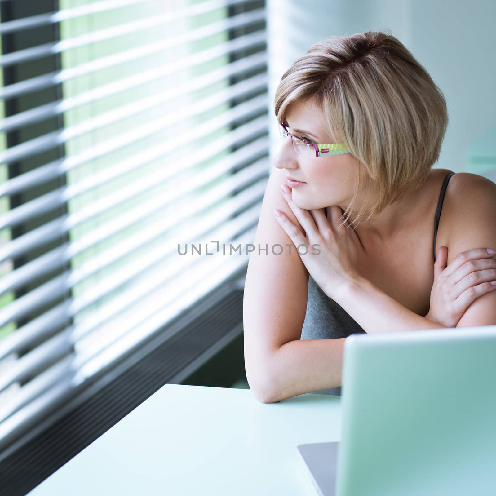 Portrait of a young woman pensively looking out of the window while sitting in front of her laptop