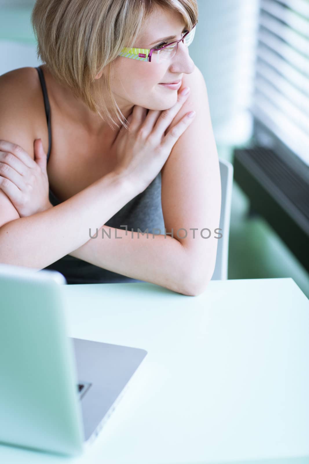 Portrait of a young woman pensively looking out of the window while sitting in front of her laptop