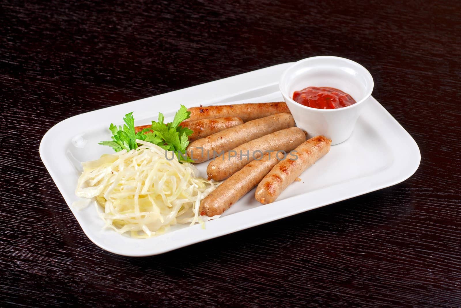 Grilled sausages with cabbage, greens and tomato sauce on white plate