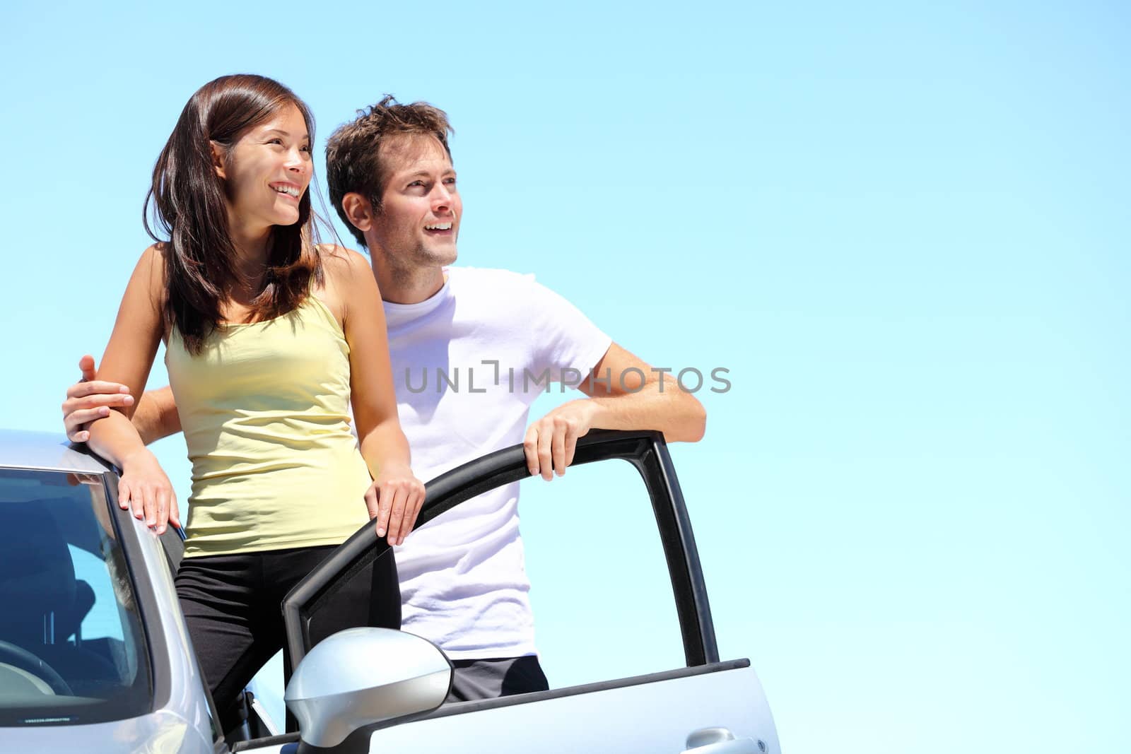 Happy couple with car. Young interracial couple standing with car looking at the sky with copy space.