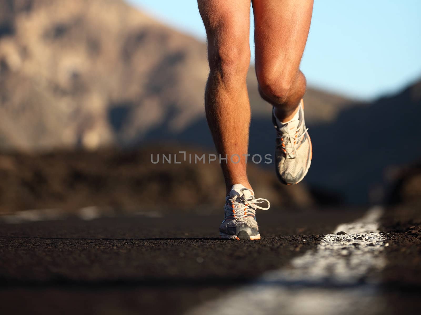 Sport running shoes in action. Closeup of male runner legs and sports shoes. Fitness man running on mountain road.