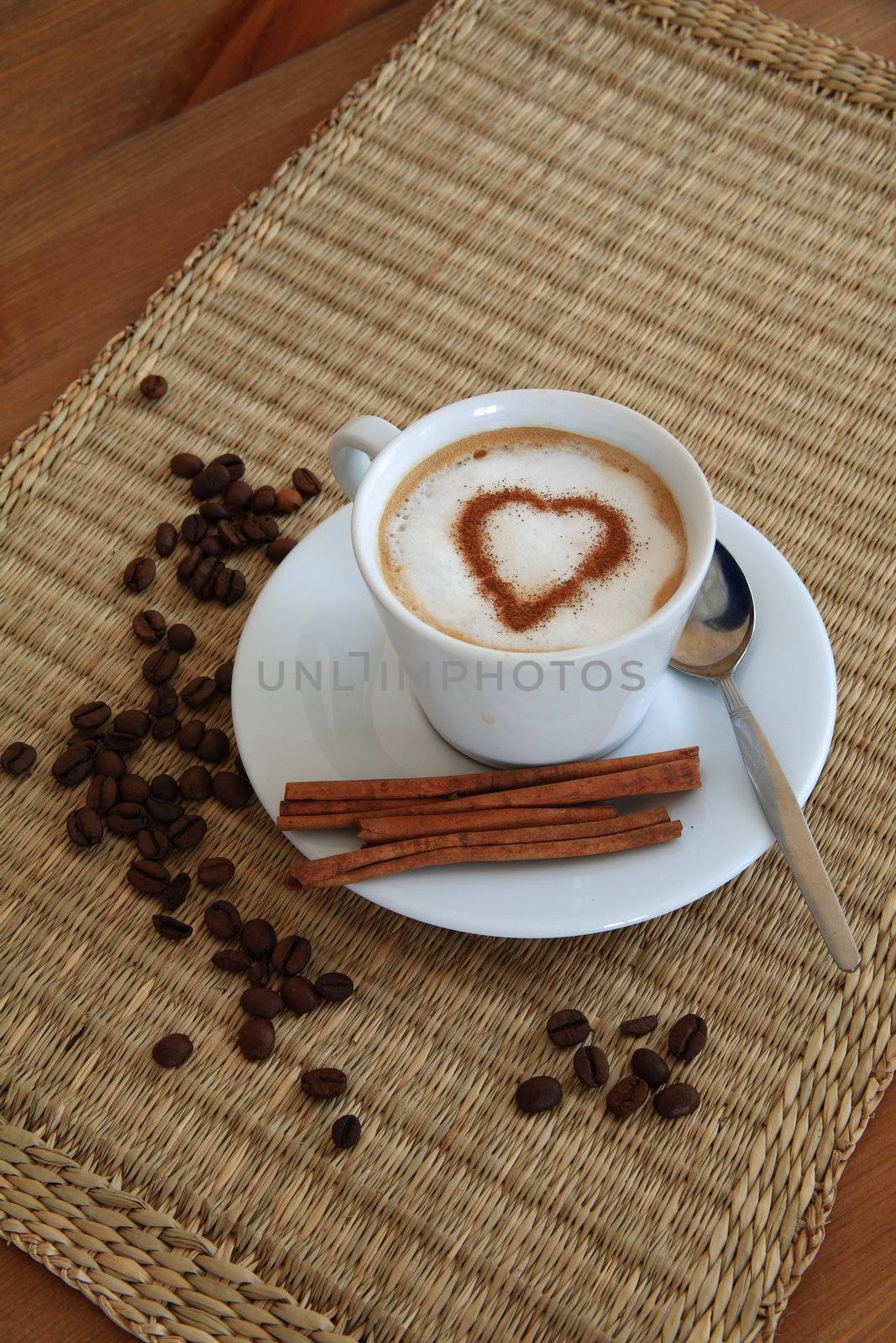 Coffee in white porcelain cup with cinnamon and roasted beans.