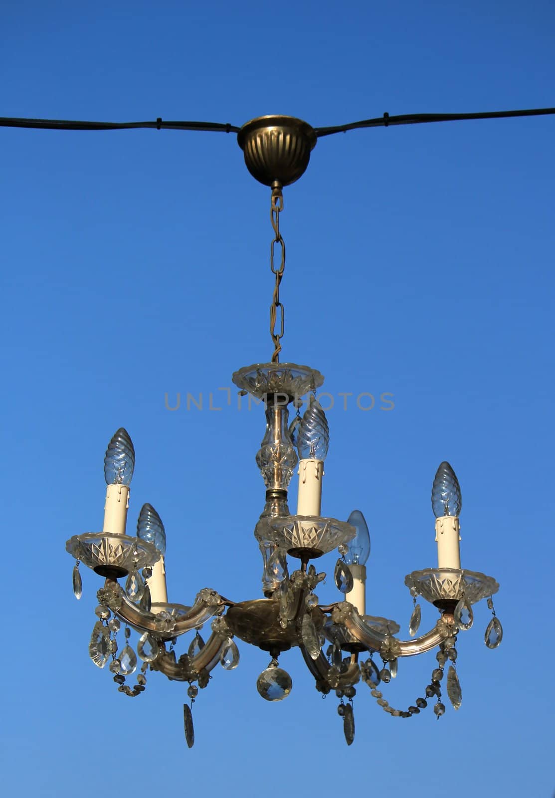 Ceiling light with five electrical candles hanging outside and blue sky in the background