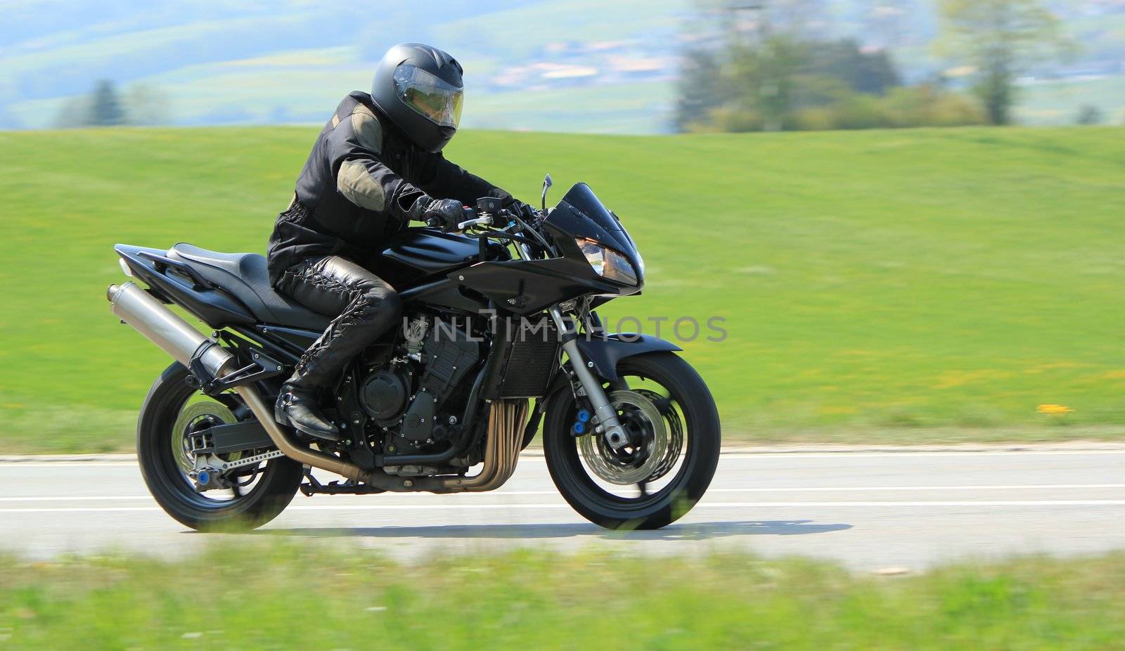 Biker wearing black clothes and driving a big motobike in the countryside